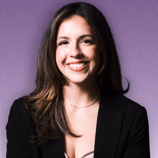 Smiling woman with long brown hair wearing a black blazer against a purple background.