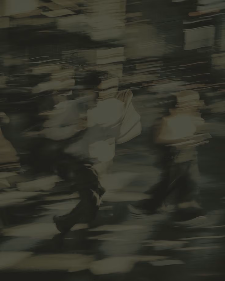 Blurred image of people walking across a city street crosswalk at night with lights in the background.