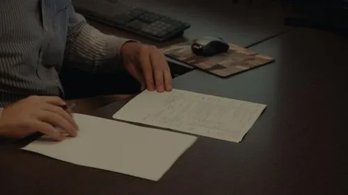 Person in striped shirt organizing papers on a dark wooden desk near a mouse and keyboard.