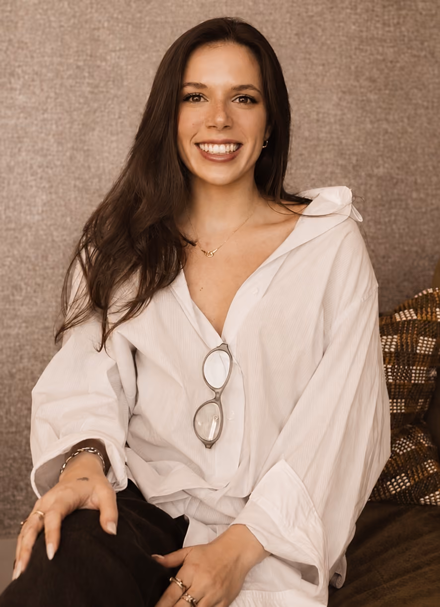 Smiling woman with long dark hair wearing a white shirt and glasses hanging from it.