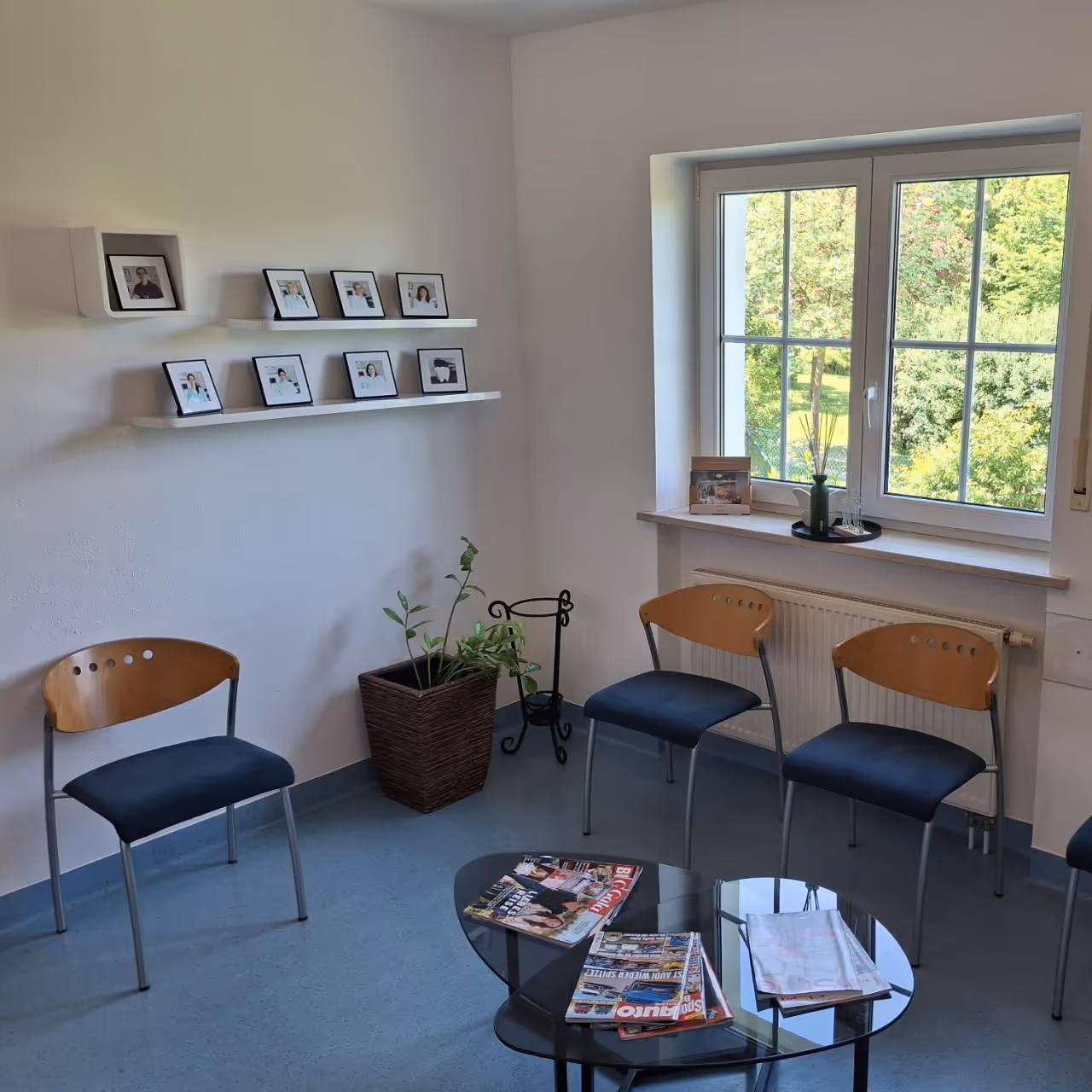Helles Wartezimmer mit fünf Holzstühlen, Fensterblick ins Grüne und Bilderrahmen an der Wand