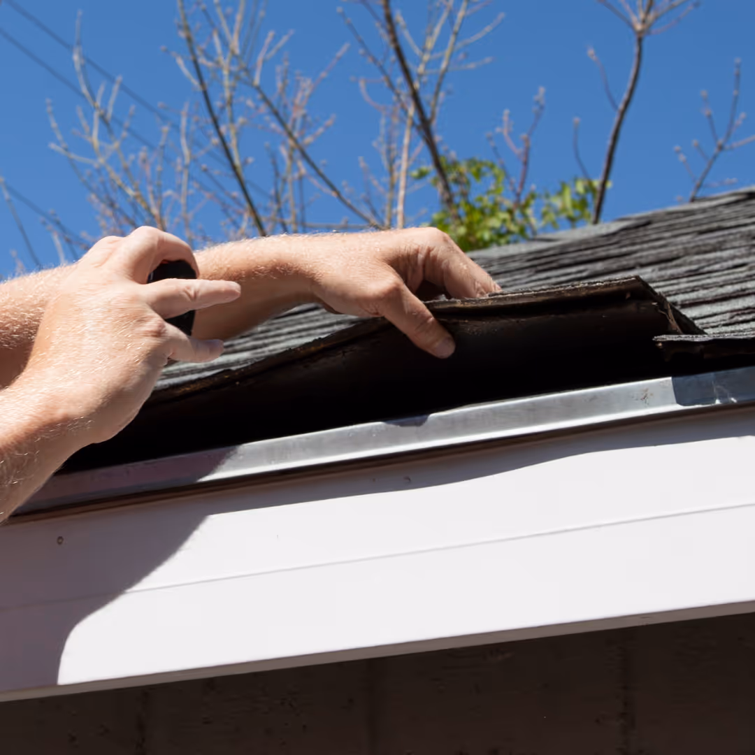 person checking damaged shingles on roof edge