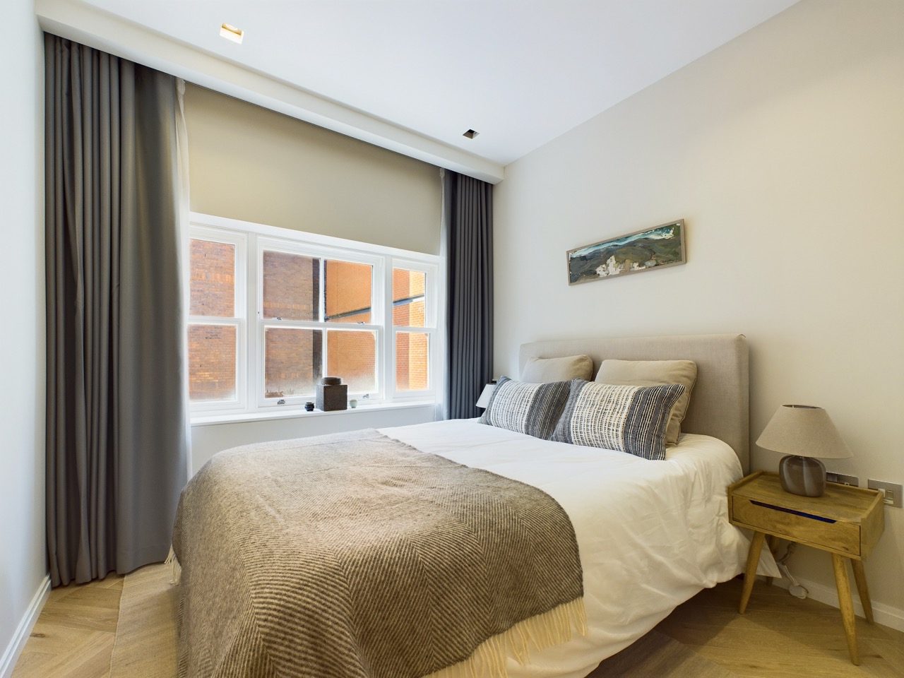 A London bedroom with neutral bedding, grey curtains and a wooden bedside table