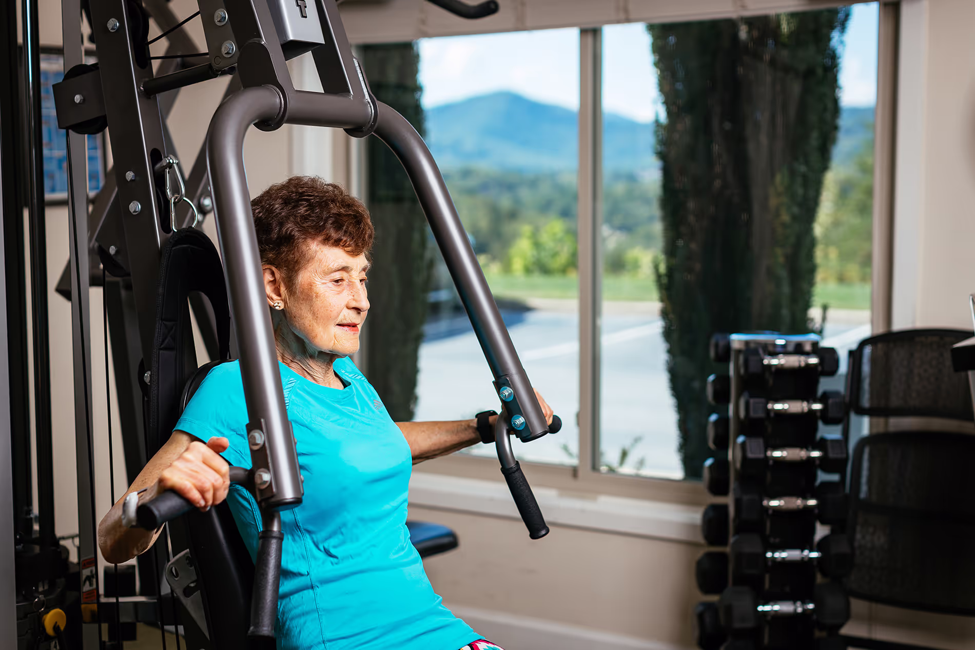 Older woman exercising on a seated chest press machine in a gym setting.