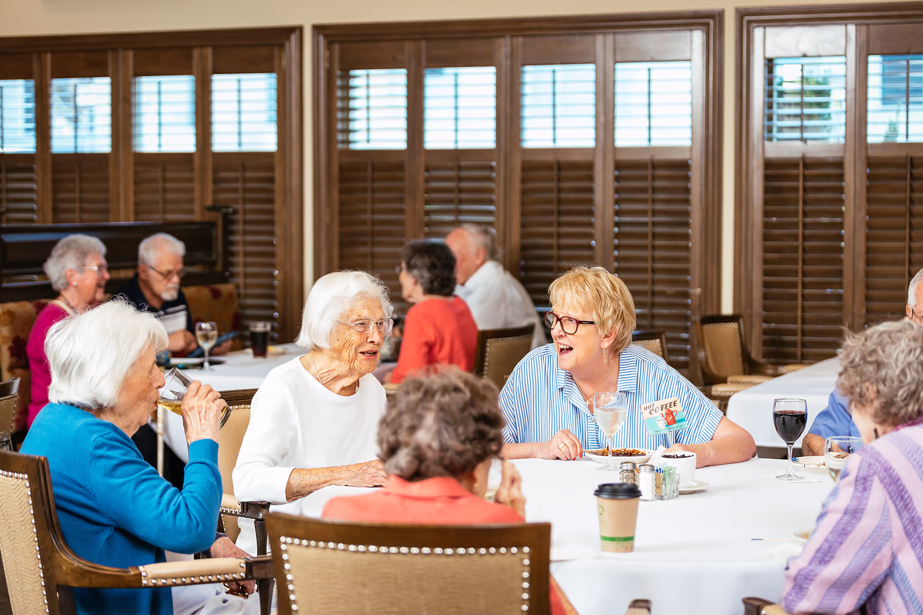 A group of seniors sitting at a table, talking and enjoying beverages in a community setting.
