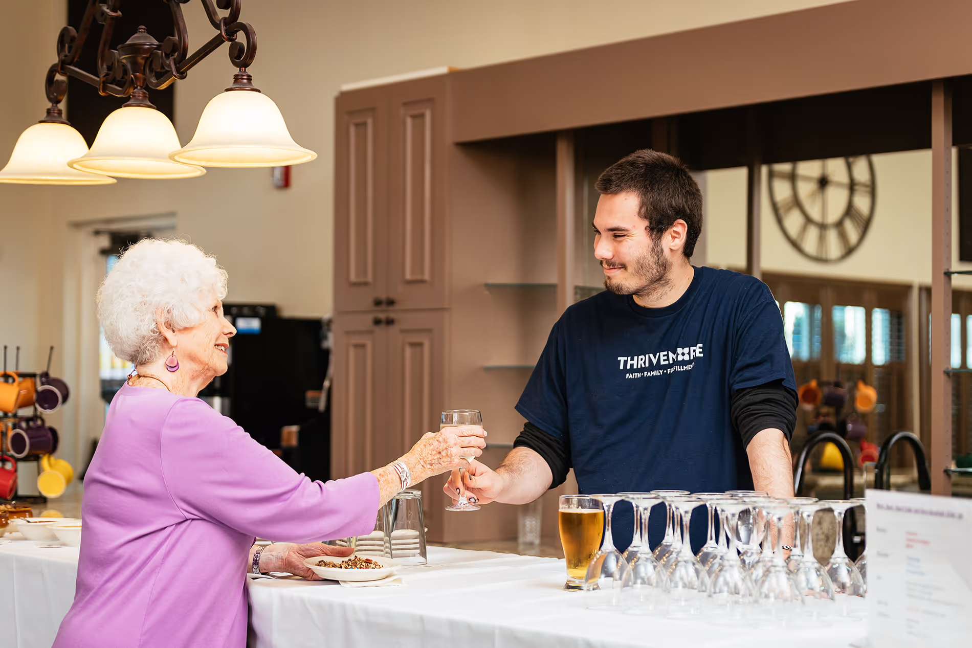 A woman and a man exchange drinks over a kitchen counter in a casual setting.