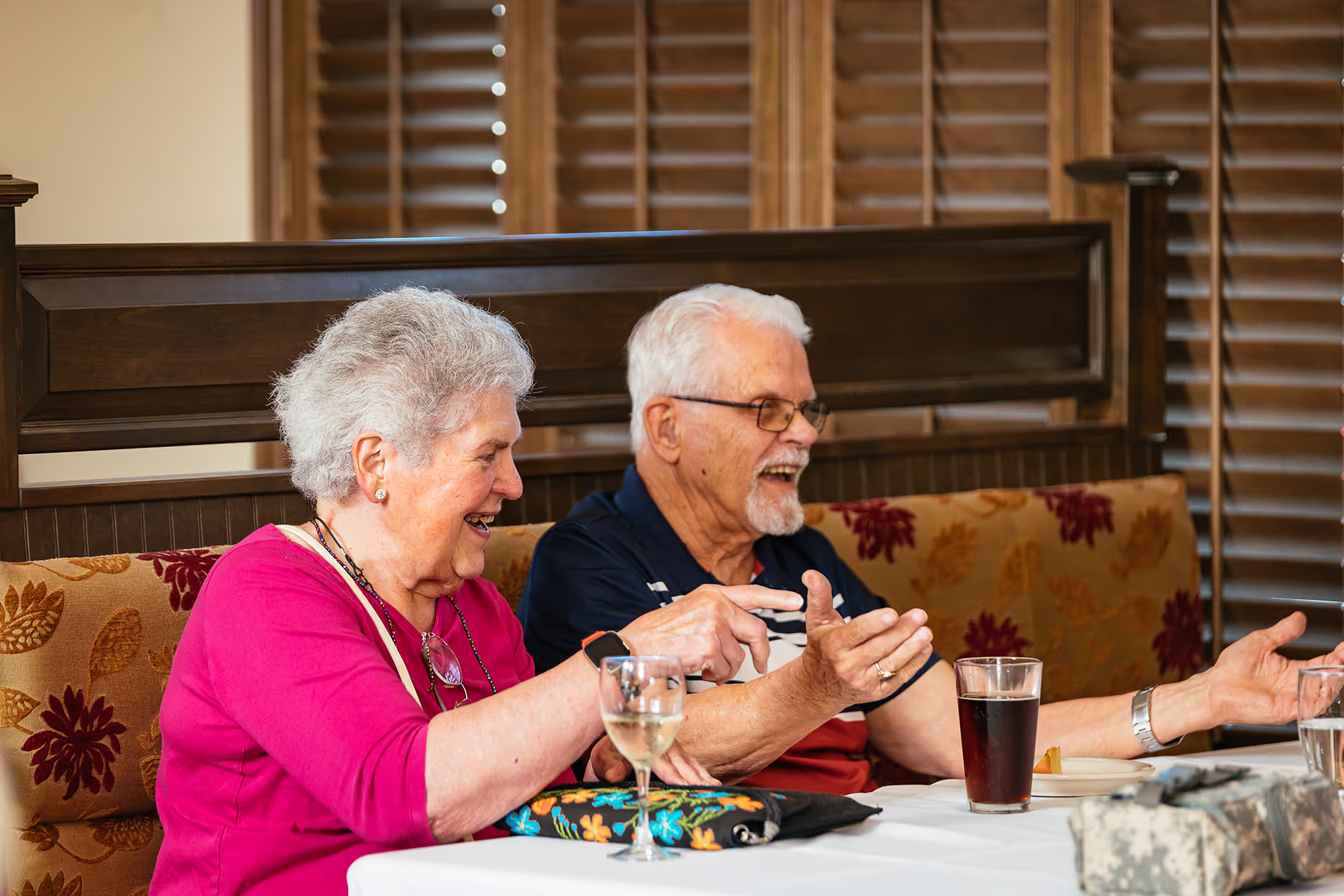 Elderly couple sitting at a table, smiling and chatting with each other.