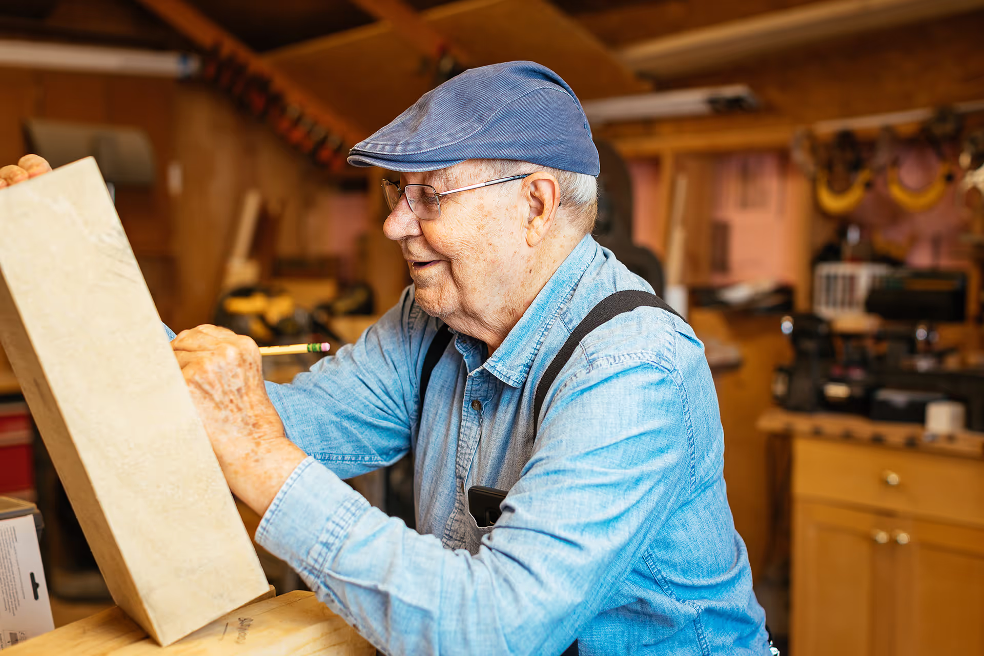 Elderly man wearing a cap works on a wooden piece in a workshop.