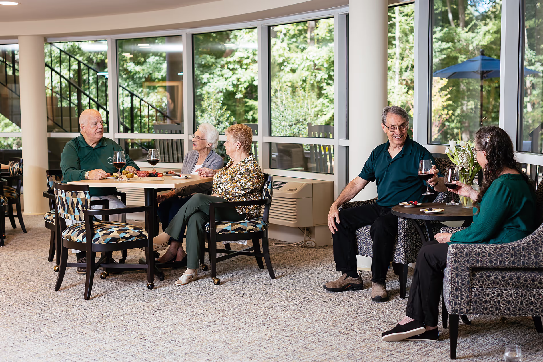 Five people seated in a room, talking and enjoying drinks around a couple of tables.