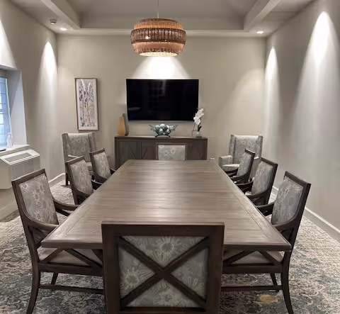 A private dining room with a long wooden table, surrounded by eight chairs, and a wall-mounted TV.