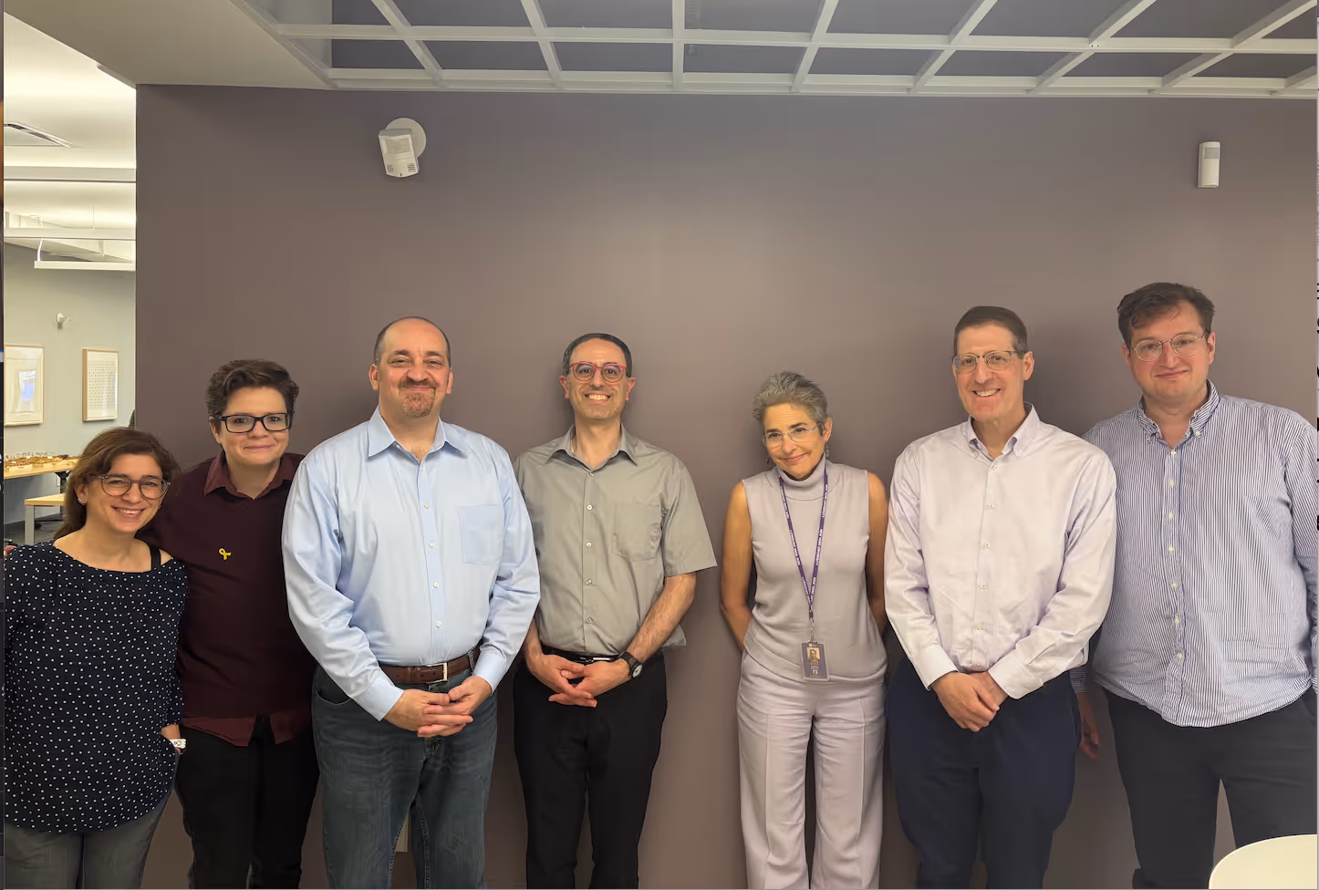 Five visiting scholars standing against gray wall smiling at camera