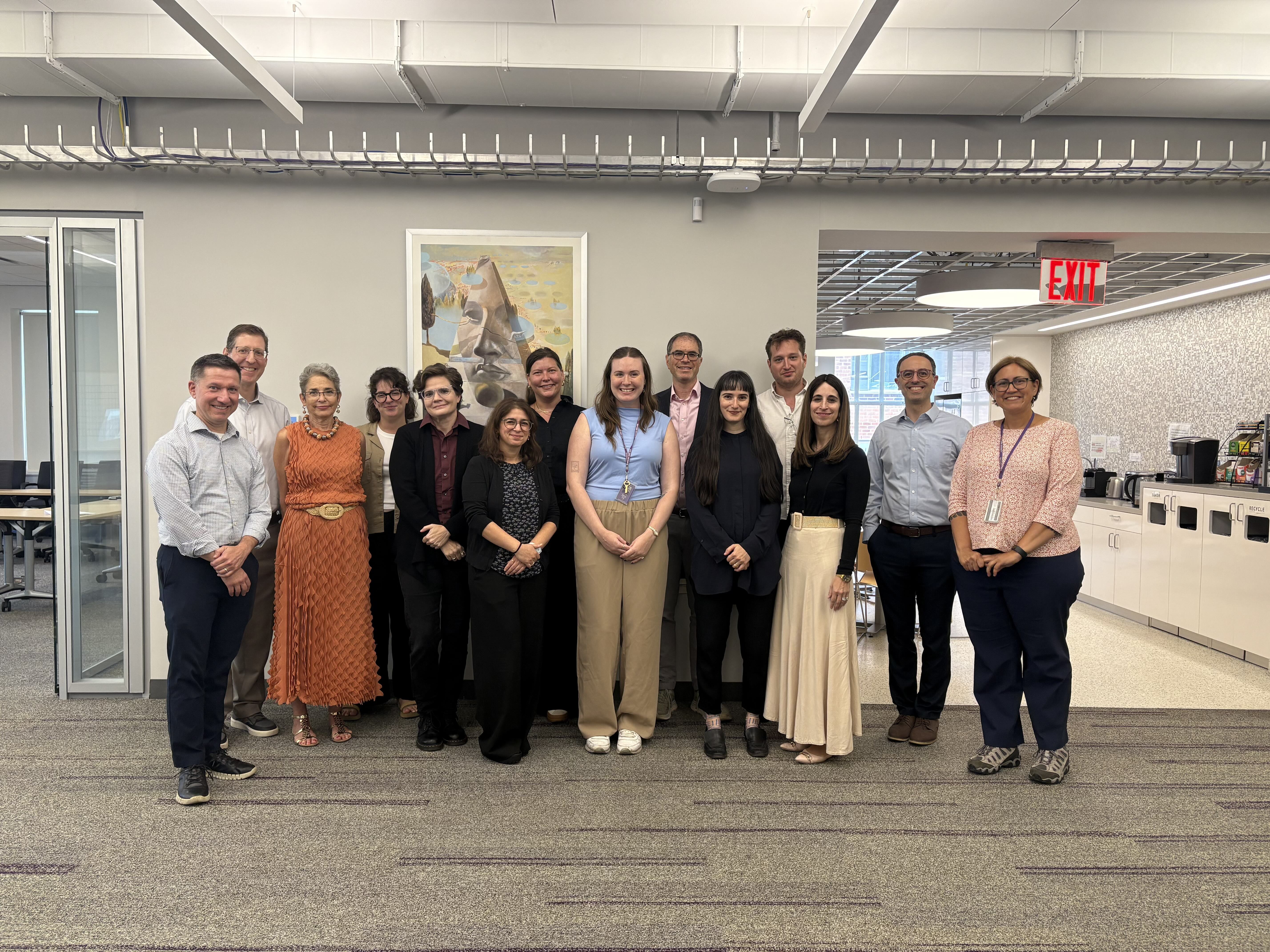 Five visiting scholars standing against gray wall smiling at camera