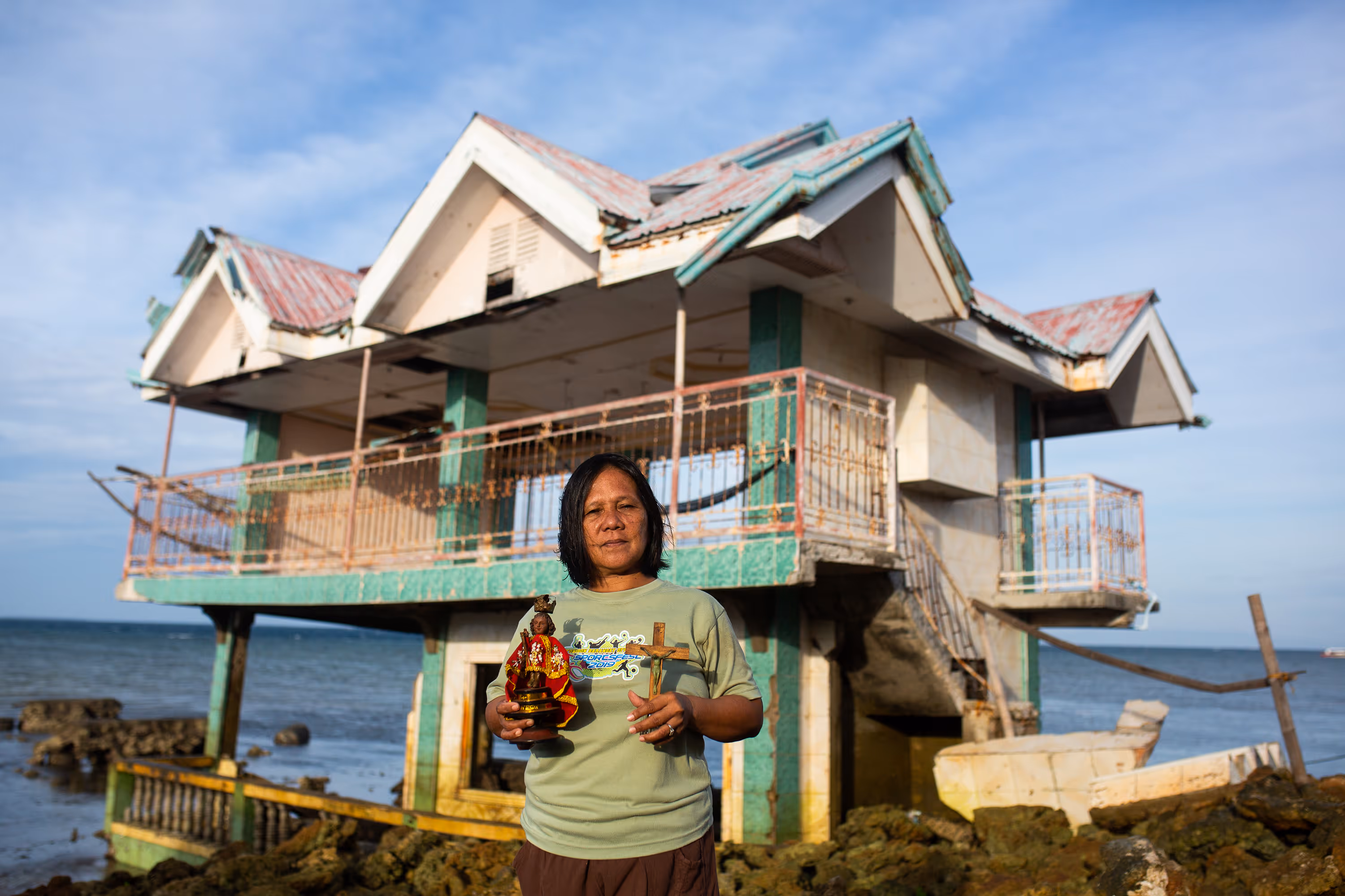 Annie, a Filipino woman, poses for a photograph in front of a structure destroyed by super Typhoon Odette in Batasan Island in Tubigon, Bohol. She holds a crucifix and a Santo Niño figure.