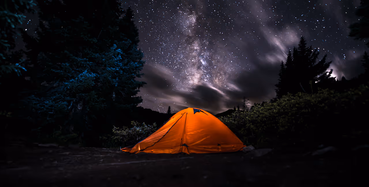 Backpacking tent glowing under starry night sky in remote wilderness
