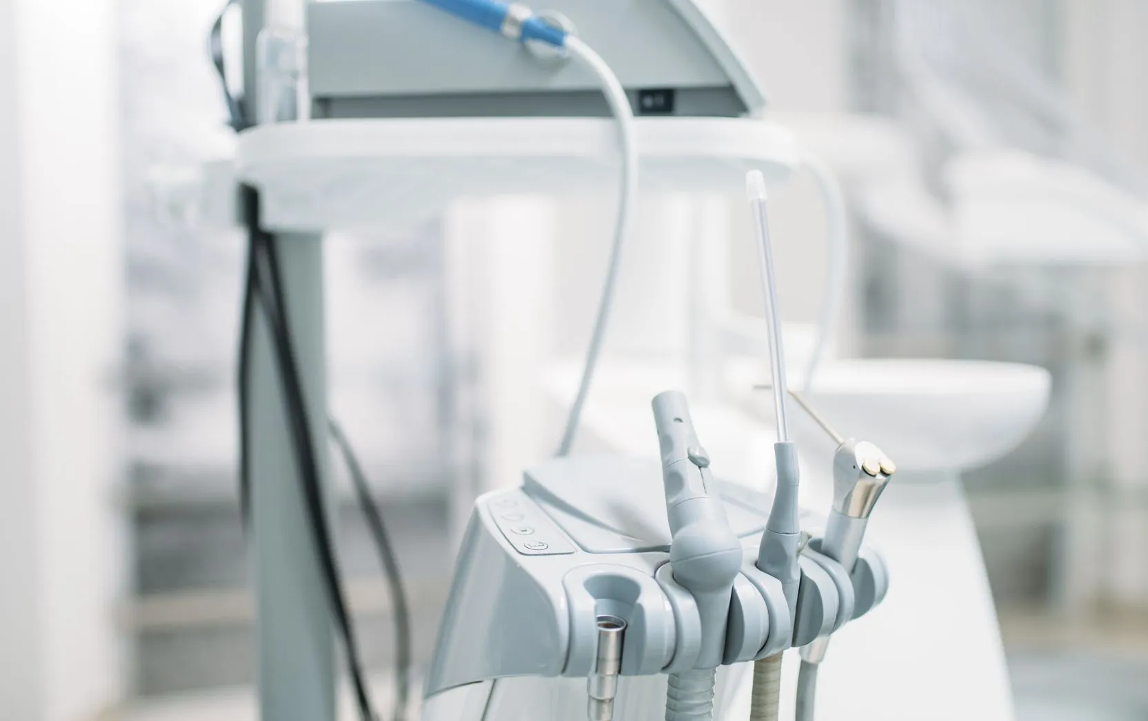 Close-up of a dental treatment cart showing multiple handpieces and hoses neatly arranged on a holder in a bright clinic.