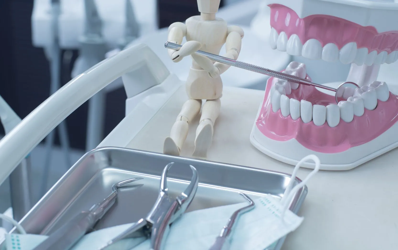 A tray of stainless-steel dental instruments lined up beside a pink-and-white plastic model of an upper and lower dental arch.