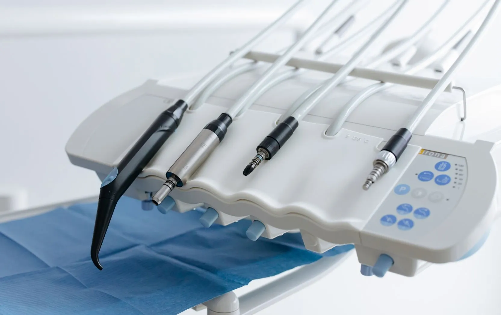 he image shows a clean and modern dental delivery system featuring a row of precision dental handpieces and instruments neatly arranged on a white control console, with clear tubing and a blue sterile drape below, reflecting the clinical efficiency and hygiene standards of a professional dental operatory