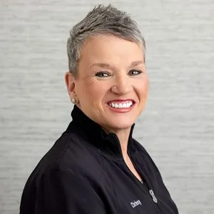 Portrait of Chrissy, specialty services manager, wearing a black zip-up jacket against a light gray background.