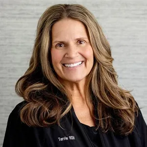 Portrait of Terrie, dental hygienist, wearing a black zip-up jacket against a light gray background.