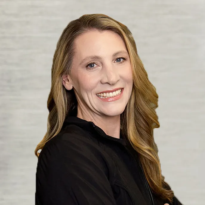 Portrait of Dr Carolyn Thompson in a black top, smiling with her head turned slightly to the side against a light gray backdrop.