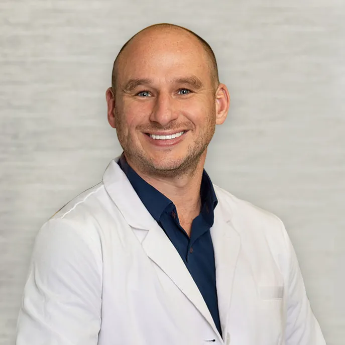Portrait of Dr Cory Fortson, wearing a white lab coat and navy shirt, smiling at the camera.