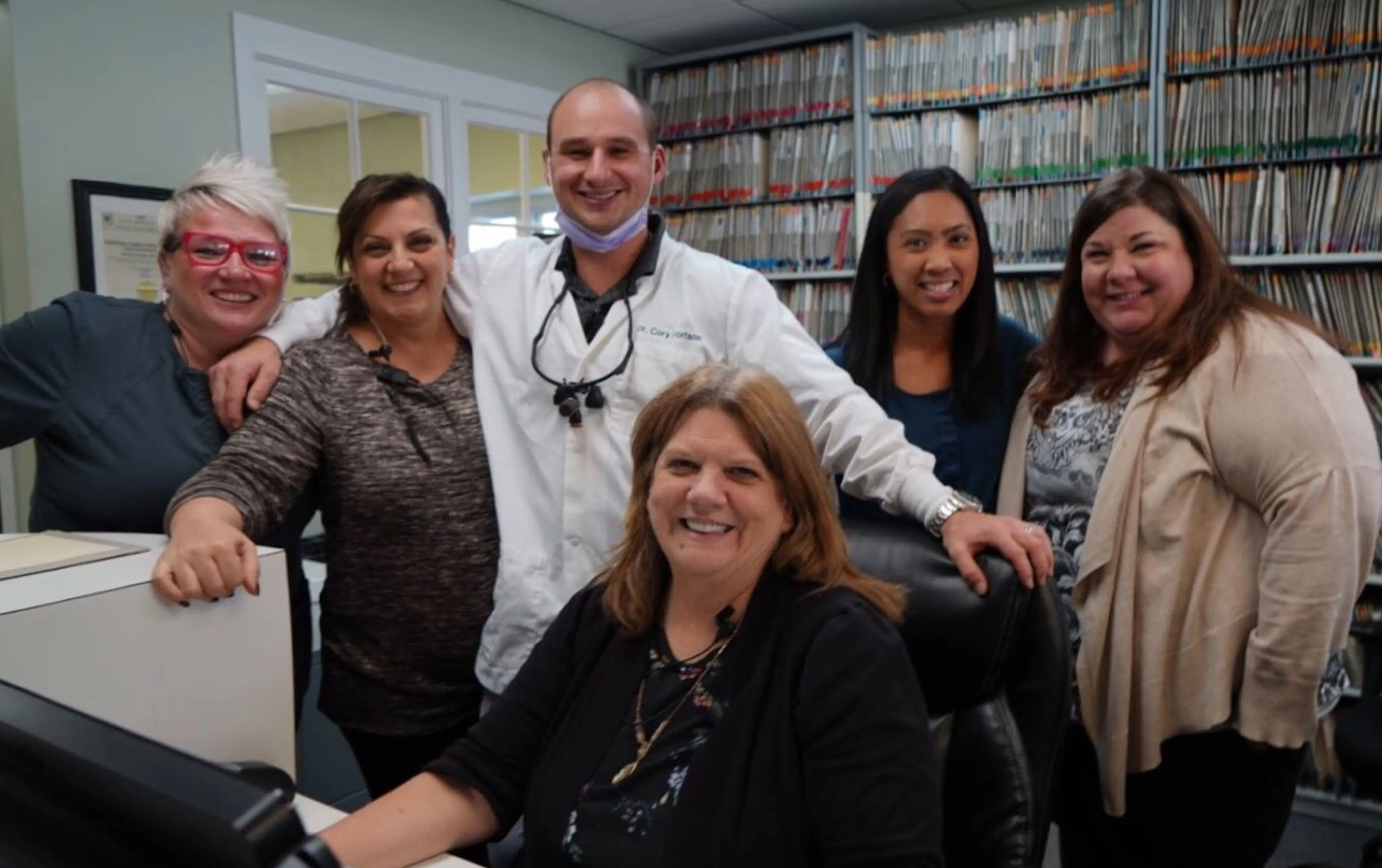 Group of dental staff and patients smiling together in a clinical environment, representing teamwork and patient care