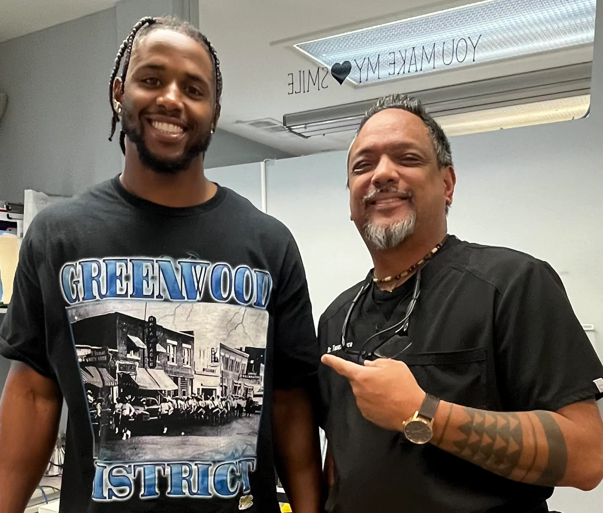 Two smiling male patients or team members standing side-by-side in a dental office, showing off successful results