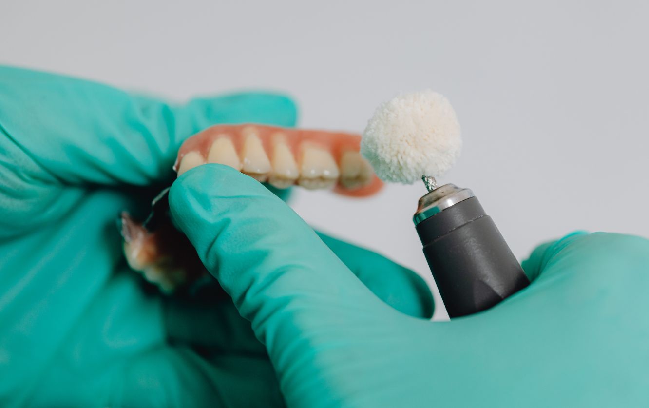 Gloved dental technician using a brush to apply ceramic layering to a metal-core dental crown during custom crown fabrication