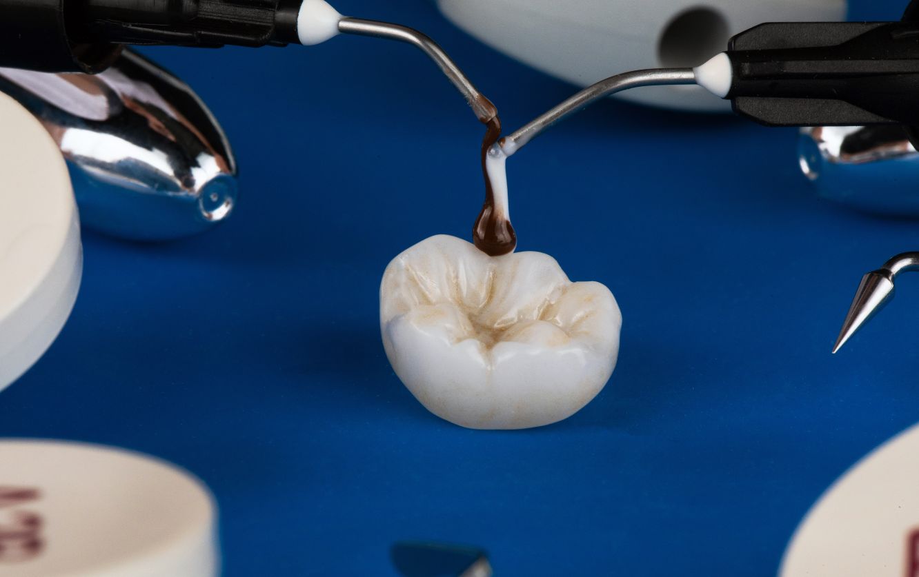 Dental lab setup showing individual ceramic crown placed on a rotating platform beside tools including dental tweezers, calipers, and ceramic powders used for shaping