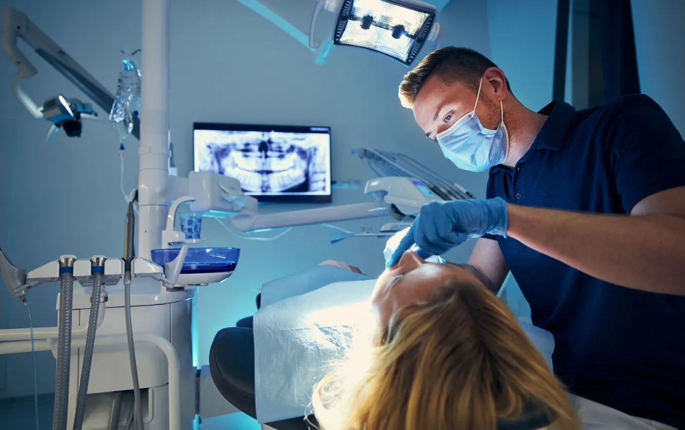 Pediatric dentist examining a child's teeth using a mirror and explorer tool during a routine dental check-up in a brightly lit, child-friendly dental office