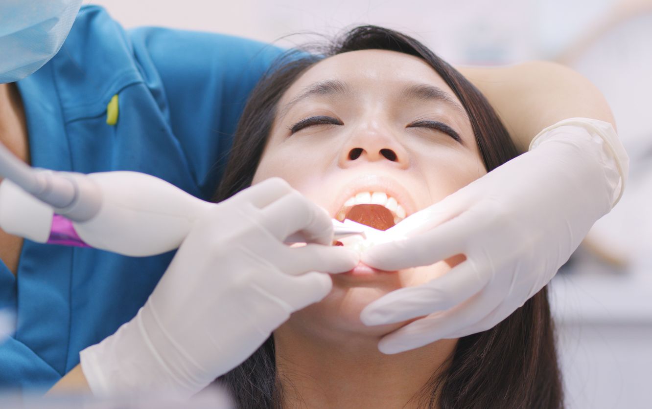 Young woman smiling while receiving a dental examination, lying comfortably in a chair as the dentist gently lifts her lip to inspect gum and tooth alignment