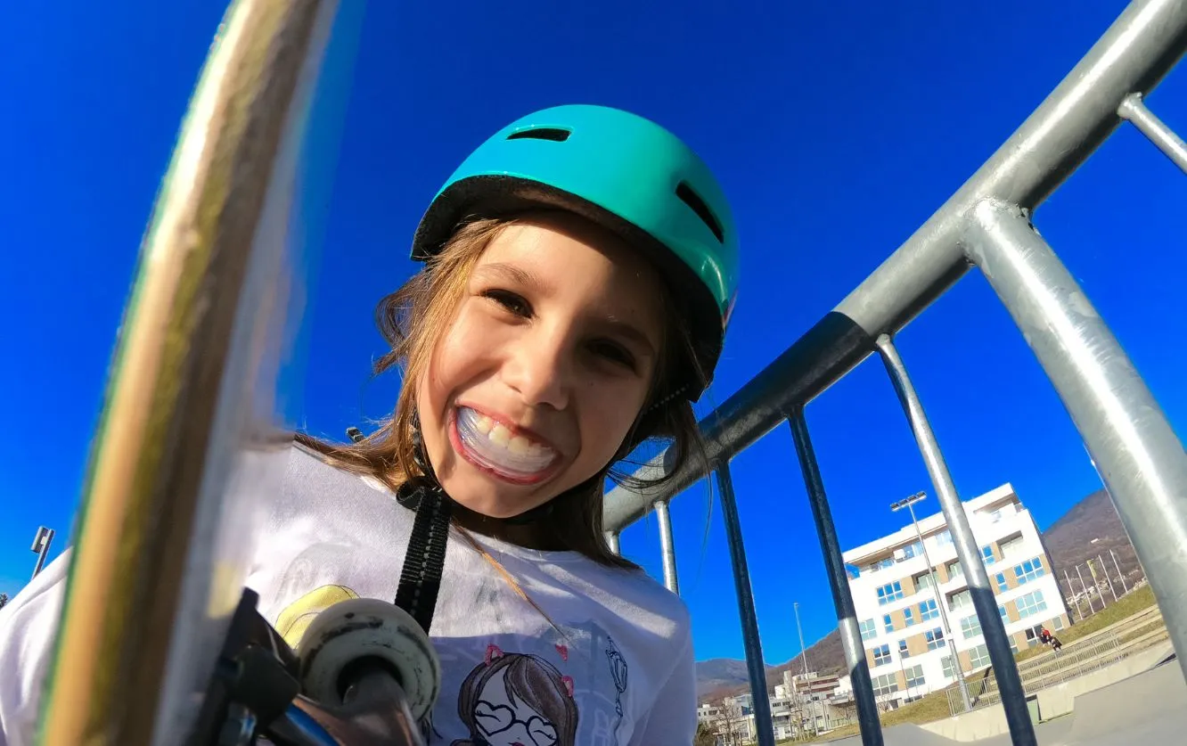 Smiling child wearing a blue helmet and outdoor jacket, captured mid-laugh on a playground, visually representing health, happiness, and confidence supported by preventative pediatric dental care