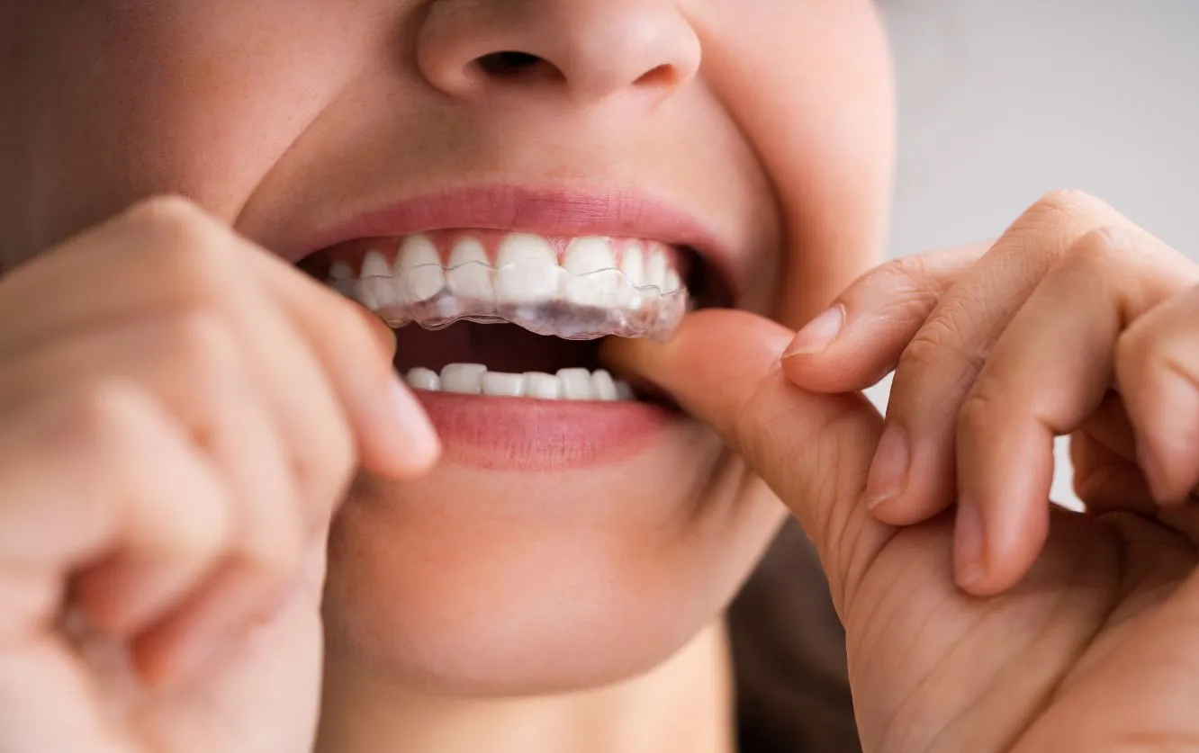 Close-up of a young woman’s hands using dental floss to clean between her upper front teeth in front of a bathroom mirror, emphasizing proper flossing technique for daily oral hygiene