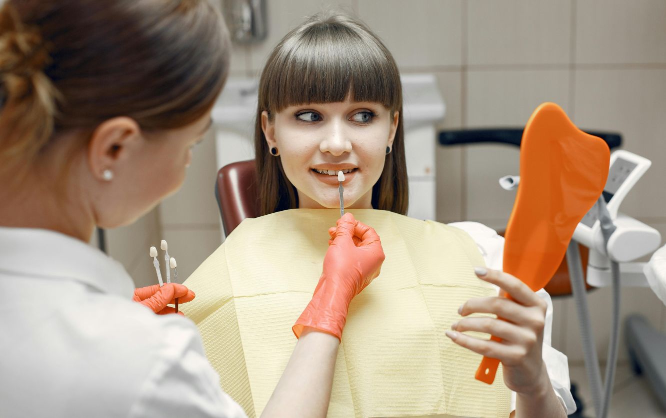 Dentist consulting with a young patient and showing a shade guide for color matching, during a cosmetic dentistry visit for veneers or teeth whitening planning