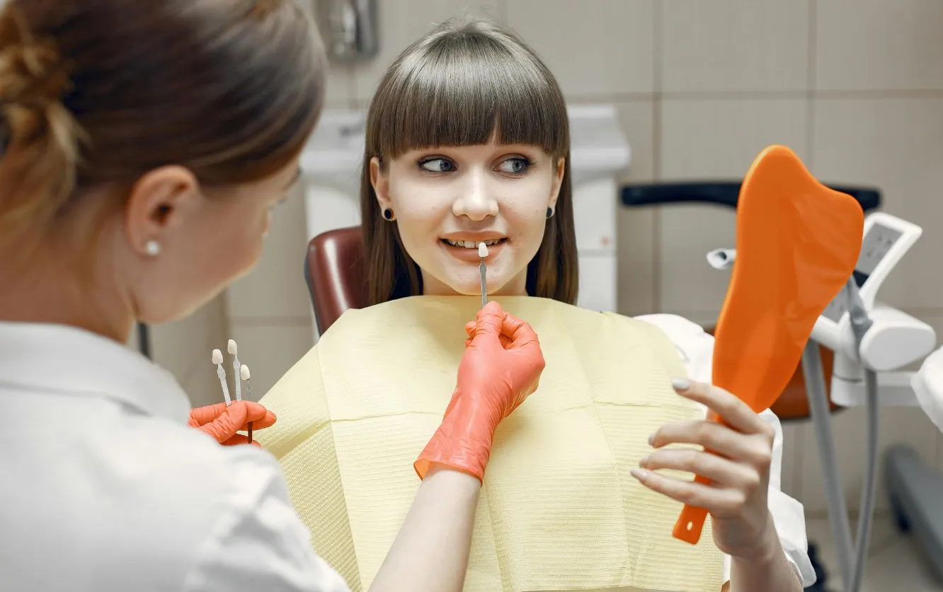 Dentist consulting with a young patient and showing a shade guide for color matching, during a cosmetic dentistry visit for veneers or teeth whitening planning