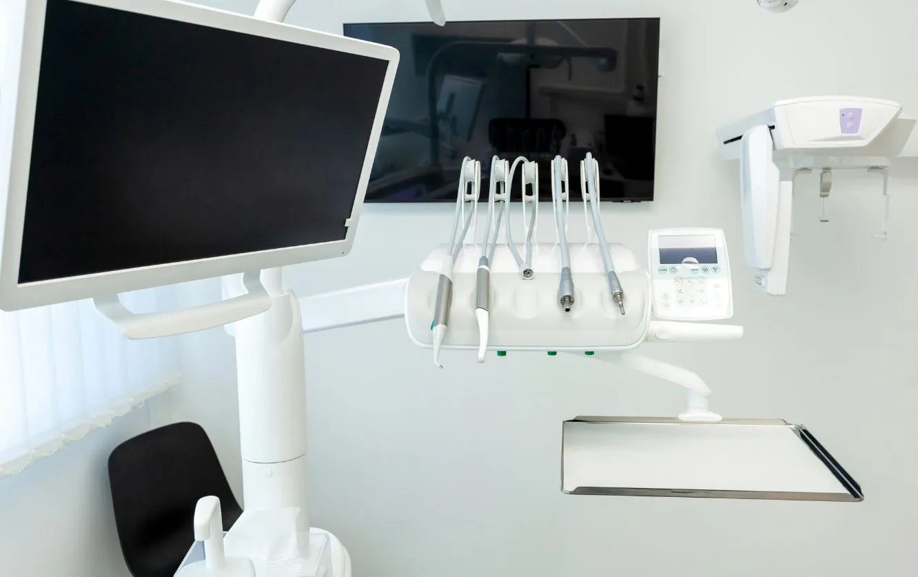 Modern dental operatory with white cabinetry, overhead light, computer monitor, and advanced dental equipment arranged in a sterile environment for patient exams and treatment procedures