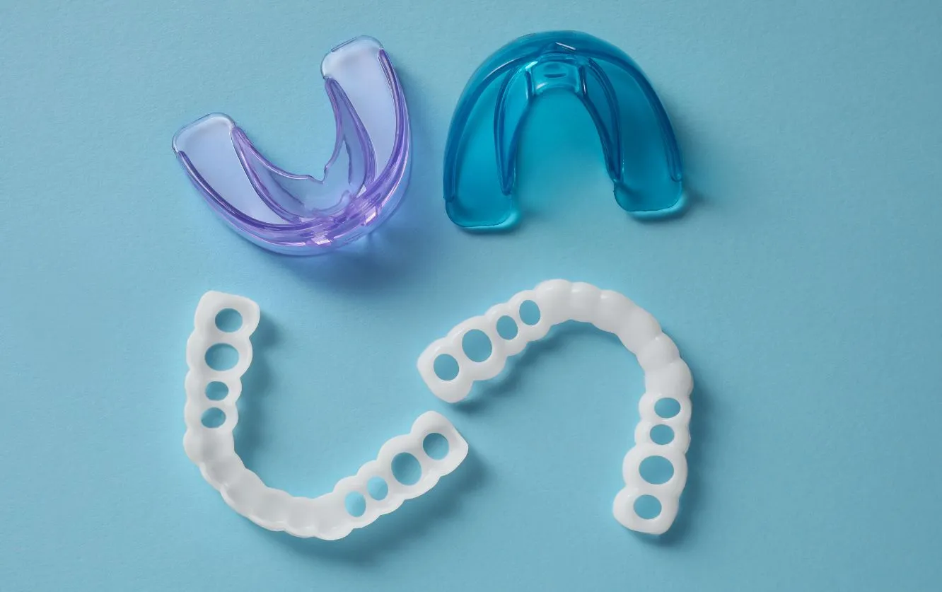 Assortment of clear orthodontic aligners and impression trays arranged on a blue background, illustrating modern clear aligner therapy options
