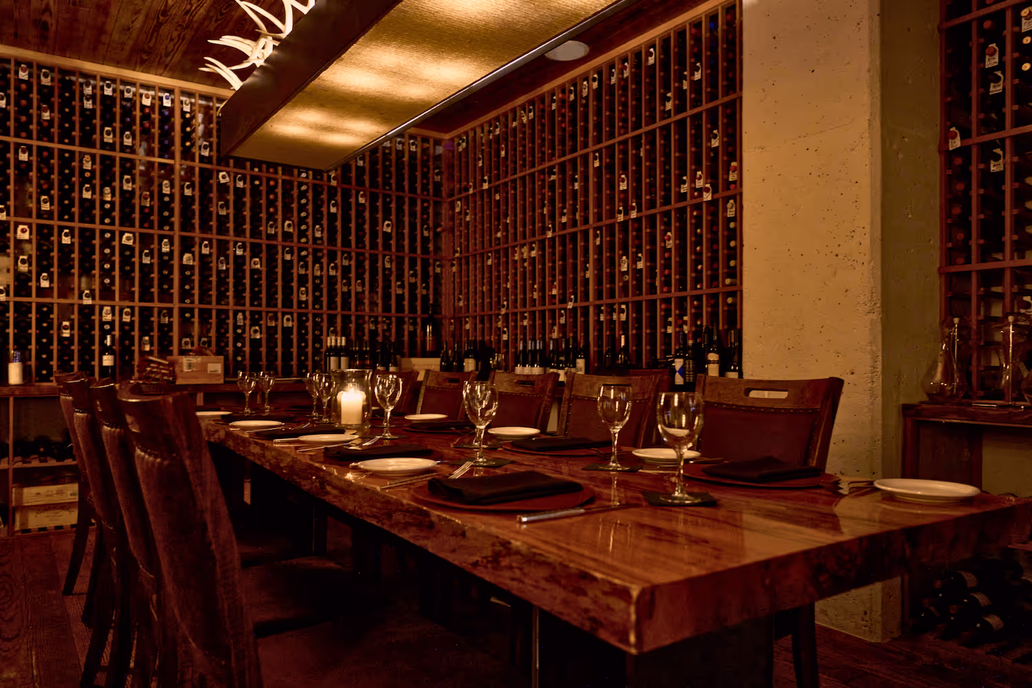 Dimly lit wine room at Lonesome Dove Austin with a long table set for dining, surrounded by wine racks.