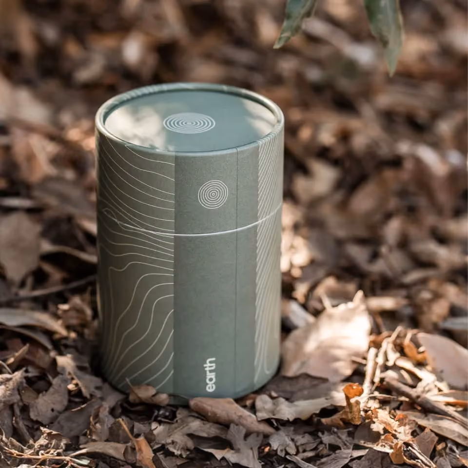 An Earth soil container sitting on a bed of leaves.