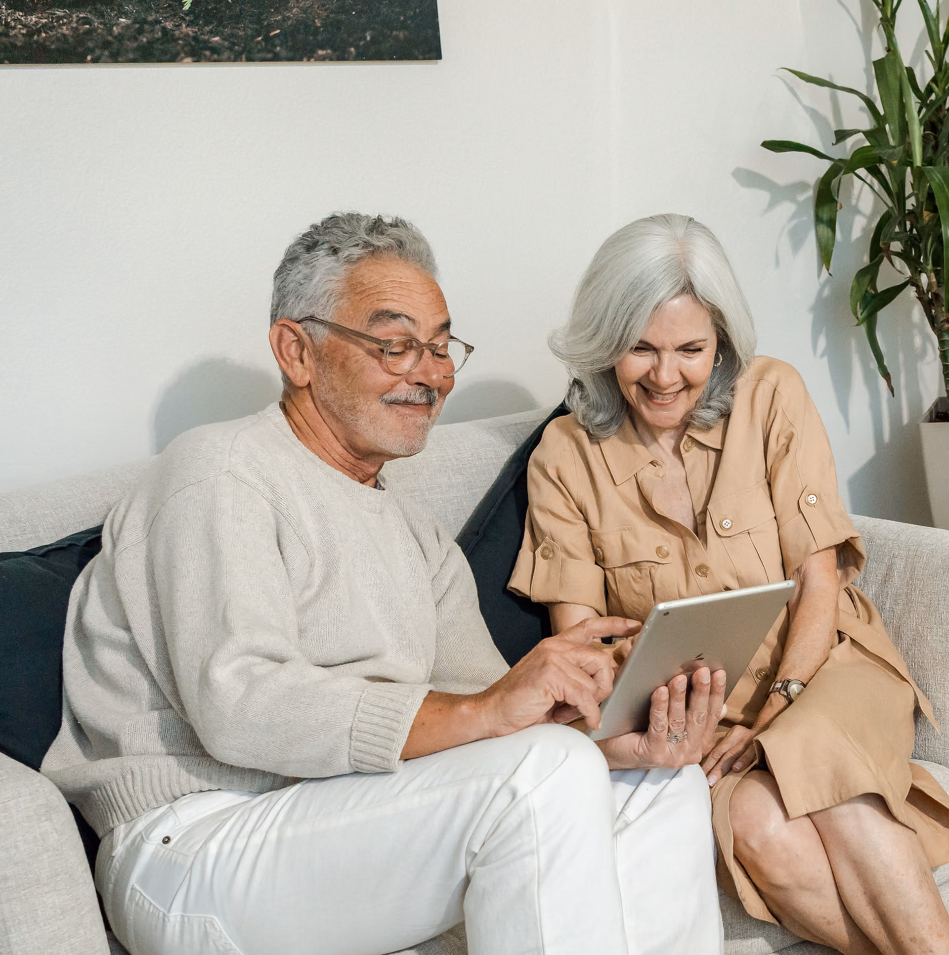 Earth Funeral - Smiling elderly couple sitting on sofa looking at a tablet together in a cozy room.