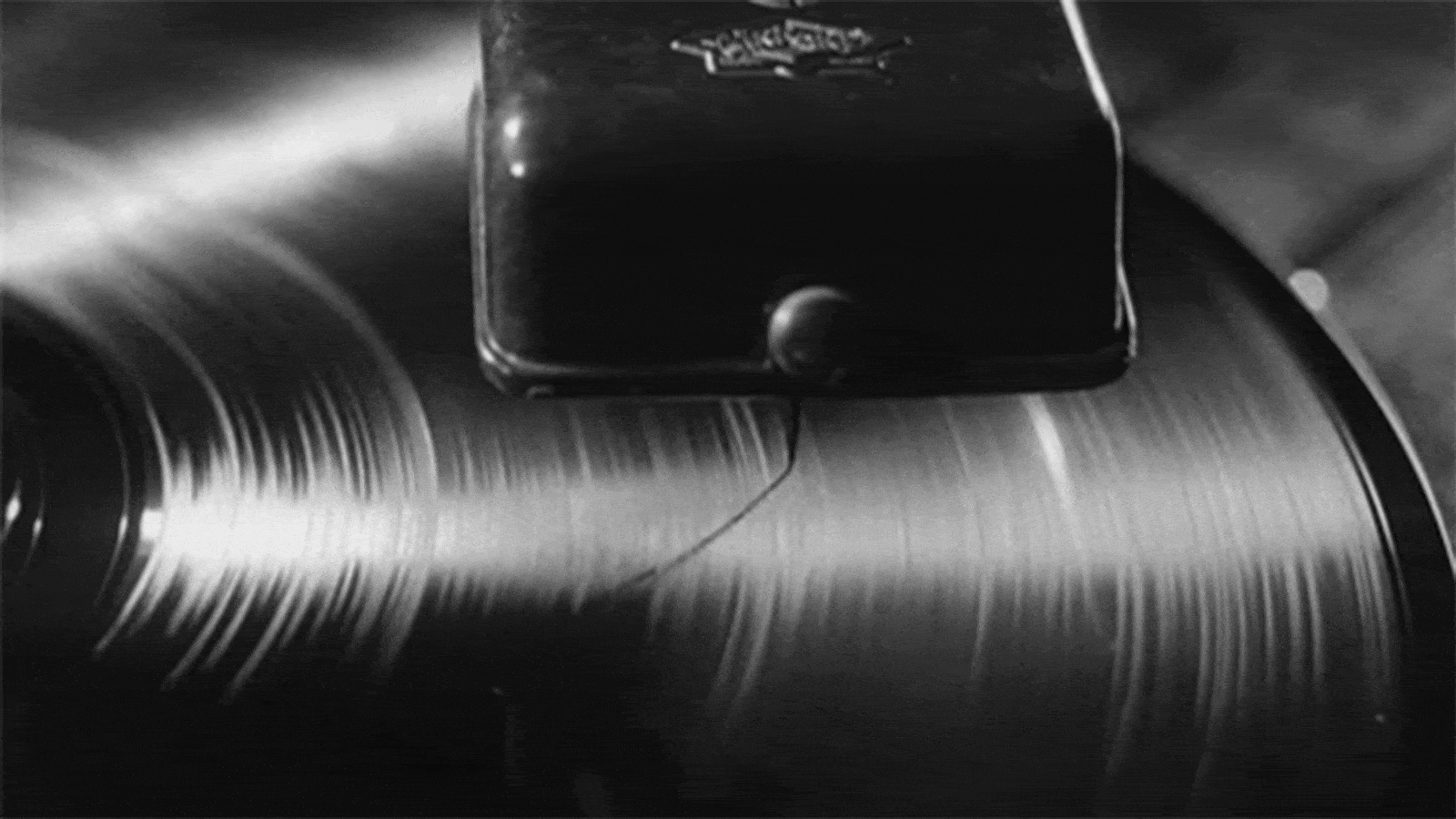 Black and white close-up of a record player needle playing a spinning vinyl record.