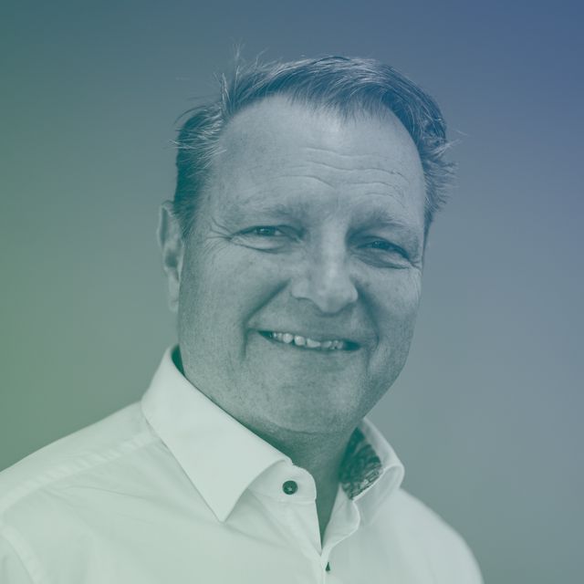 Smiling middle-aged man wearing a white collared shirt against a plain background.