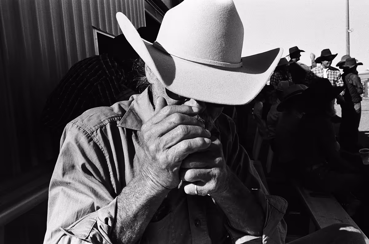 Cowboy smoking cigarette at rodeo, white hat obscuring face