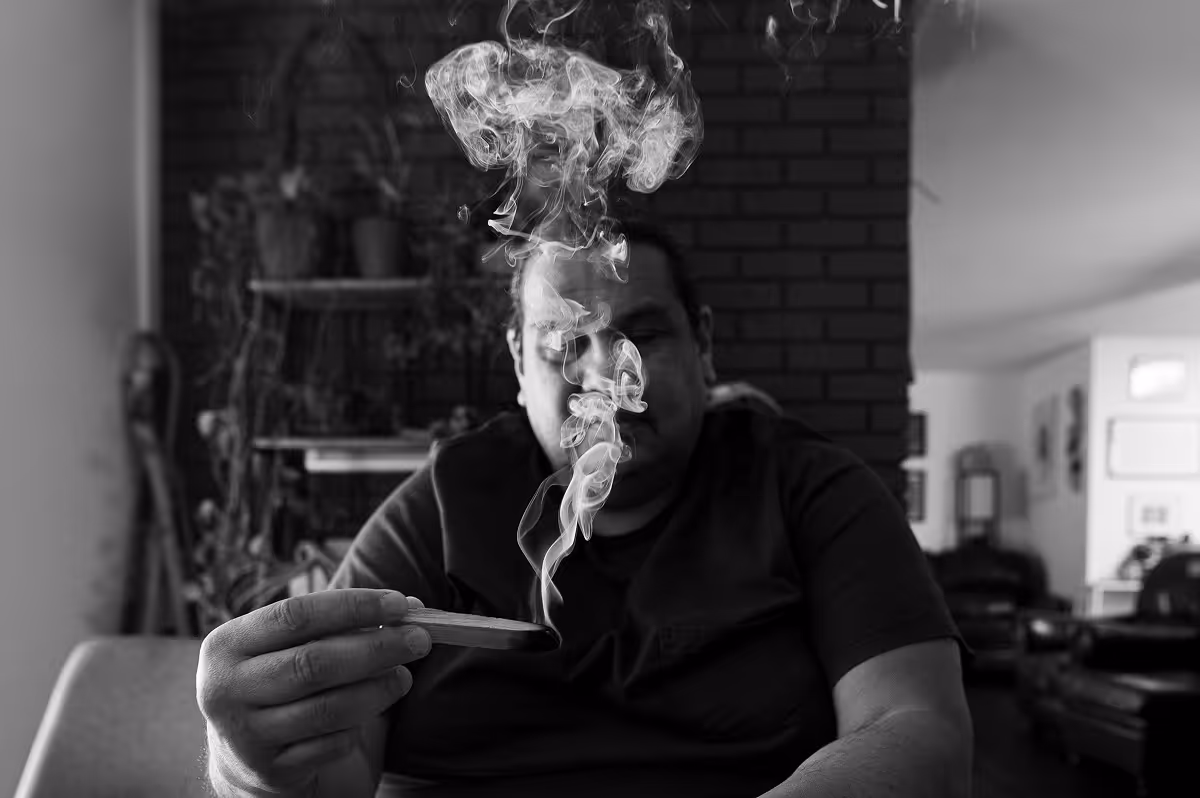 Person holding burning incense stick with smoke rising indoors