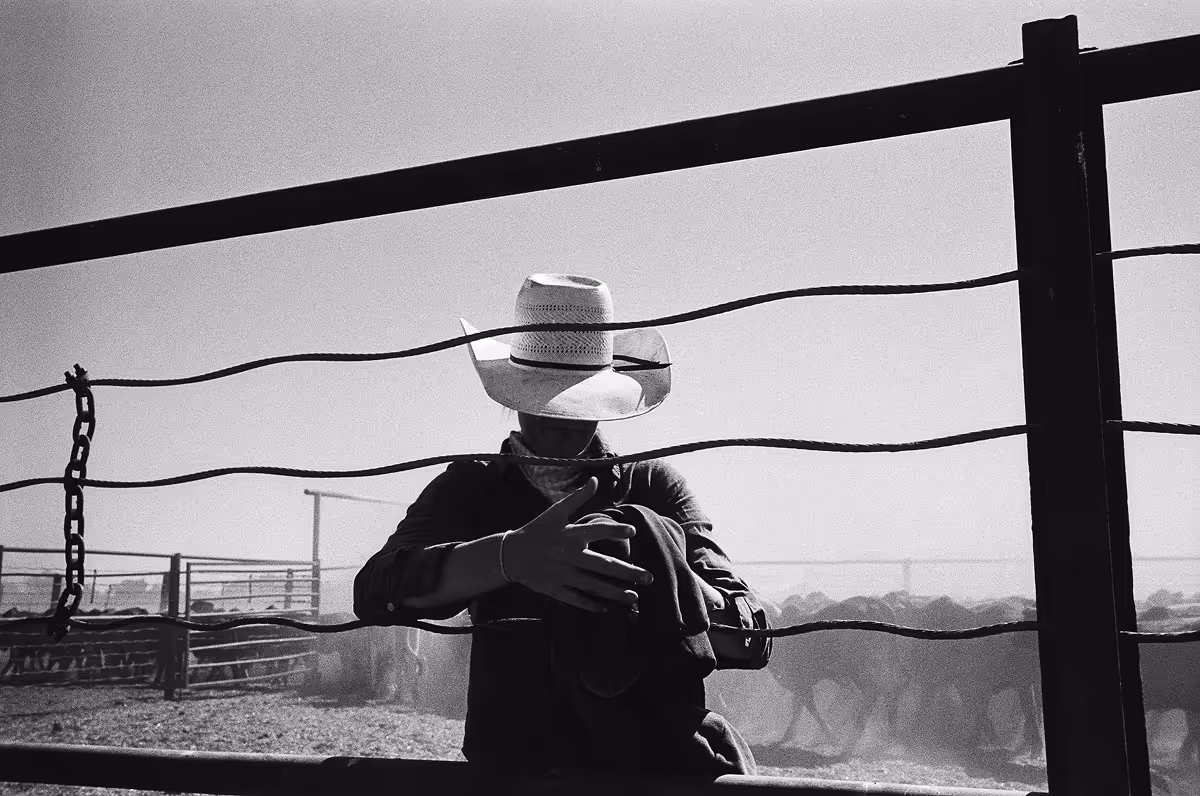 Silhouetted figure in cowboy hat leaning on fence at ranch