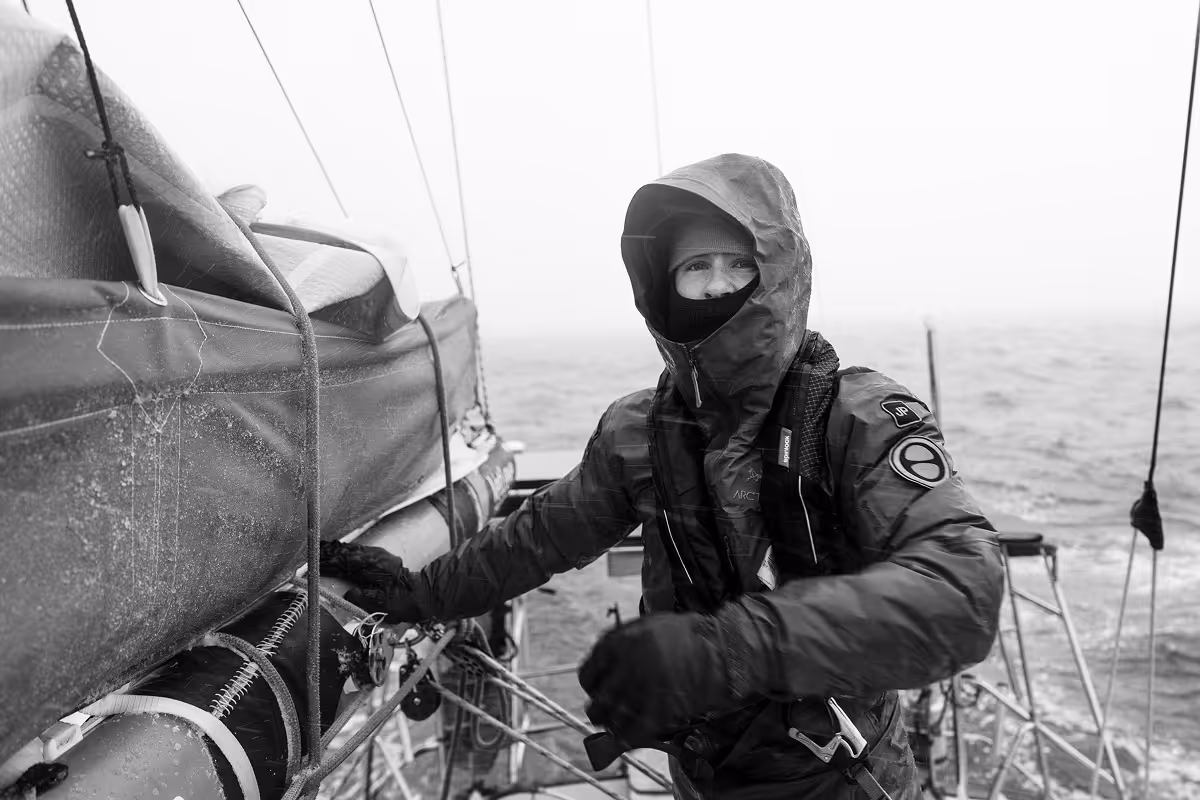 Sailor in hooded weather gear at helm during rough seas