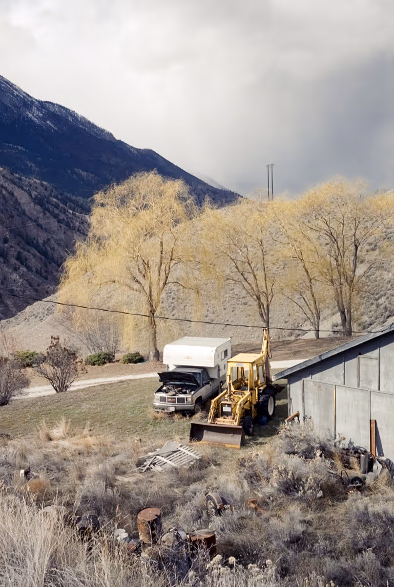 Abandoned backhoe and truck beside rural property with frost-covered trees