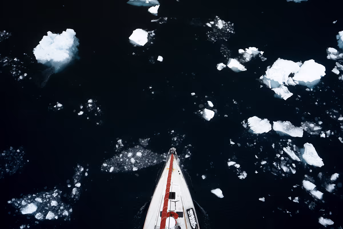 Aerial view of sailboat bow navigating through floating ice chunks in dark water