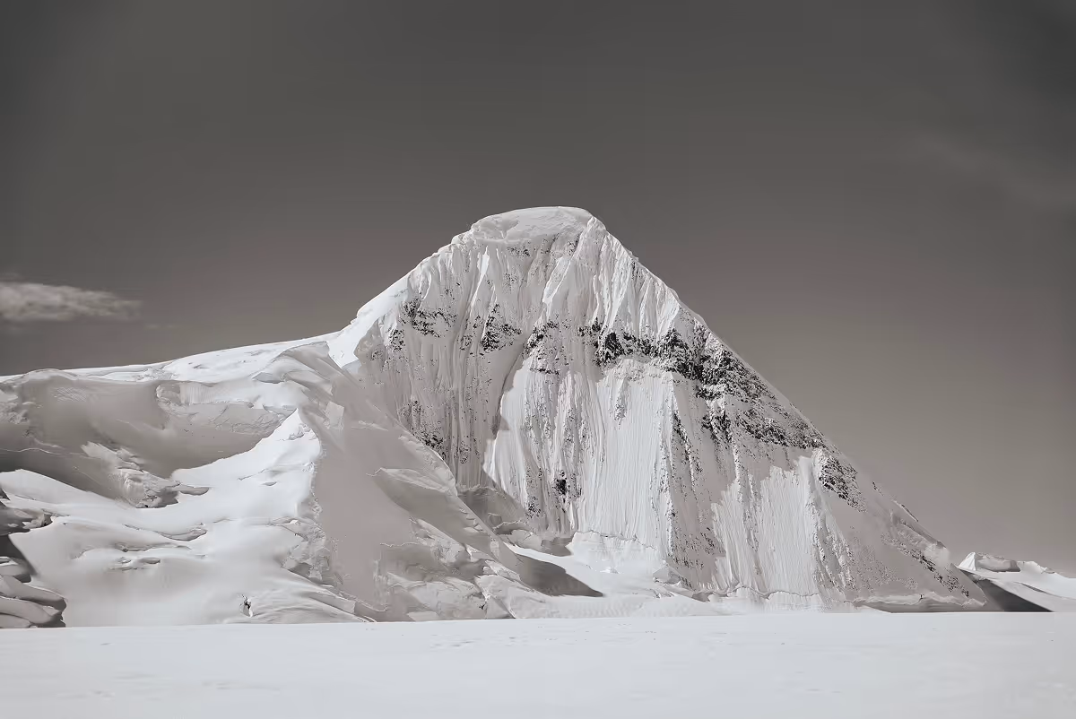 Snow-covered mountain peak with steep icy slopes under a clear gray sky.