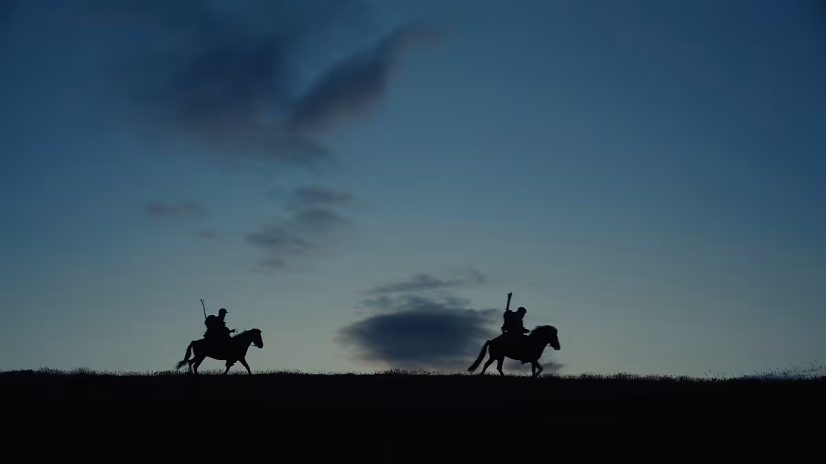 Silhouettes of two riders on horseback against a twilight sky.